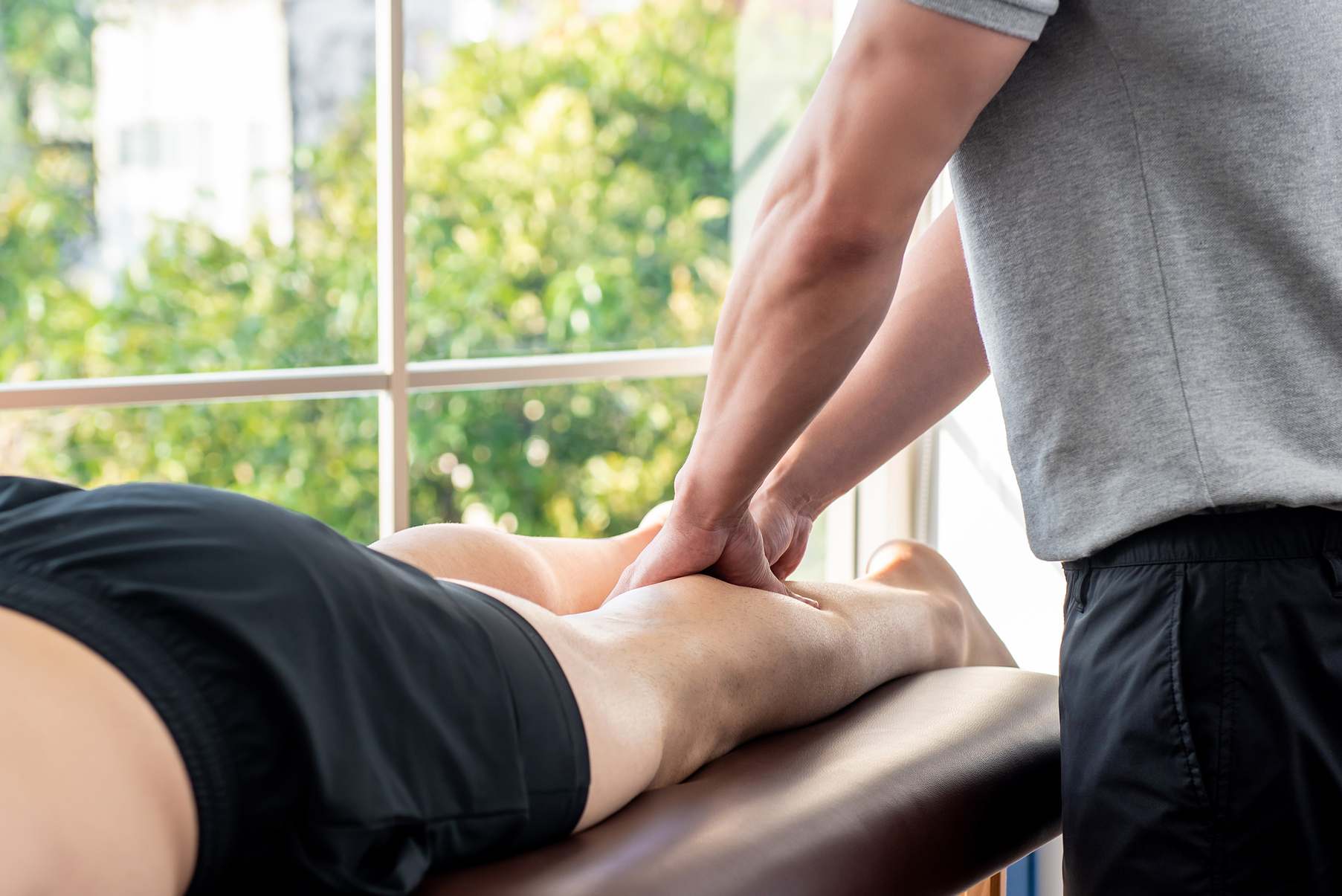 Male therapist giving leg massage to athlete patient in clinic